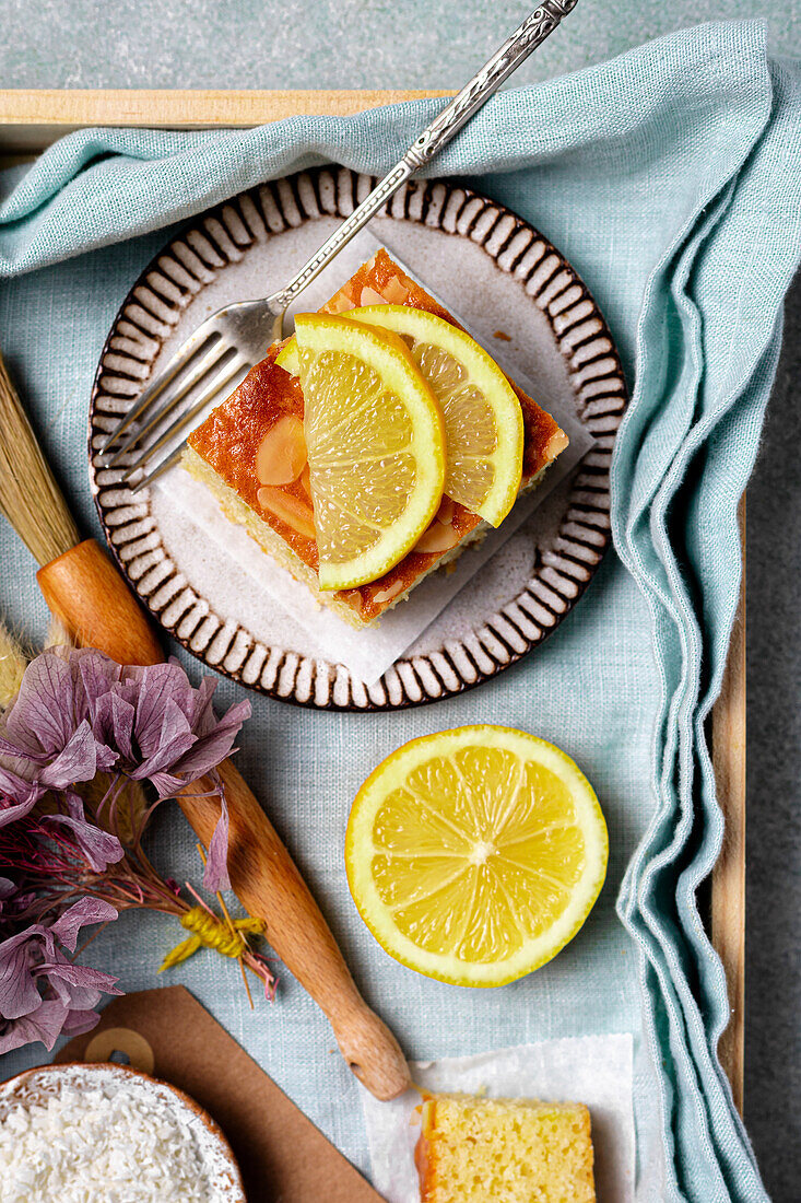 Top view of square slice of delicious homemade lemon cake served on plate with fork on tray with decorative flower