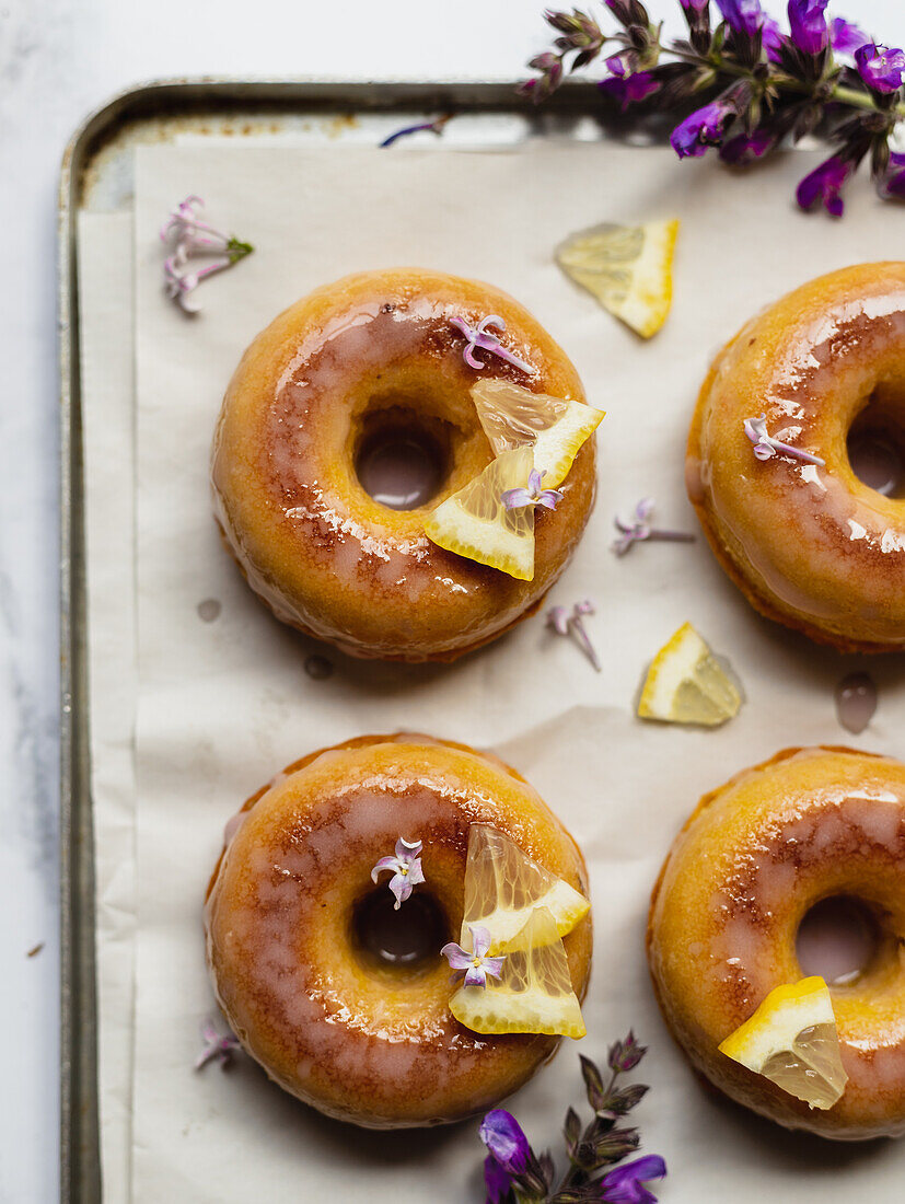 Top view of tasty donuts on cooling rack with leaves between blooming lavender sprigs on marble surface