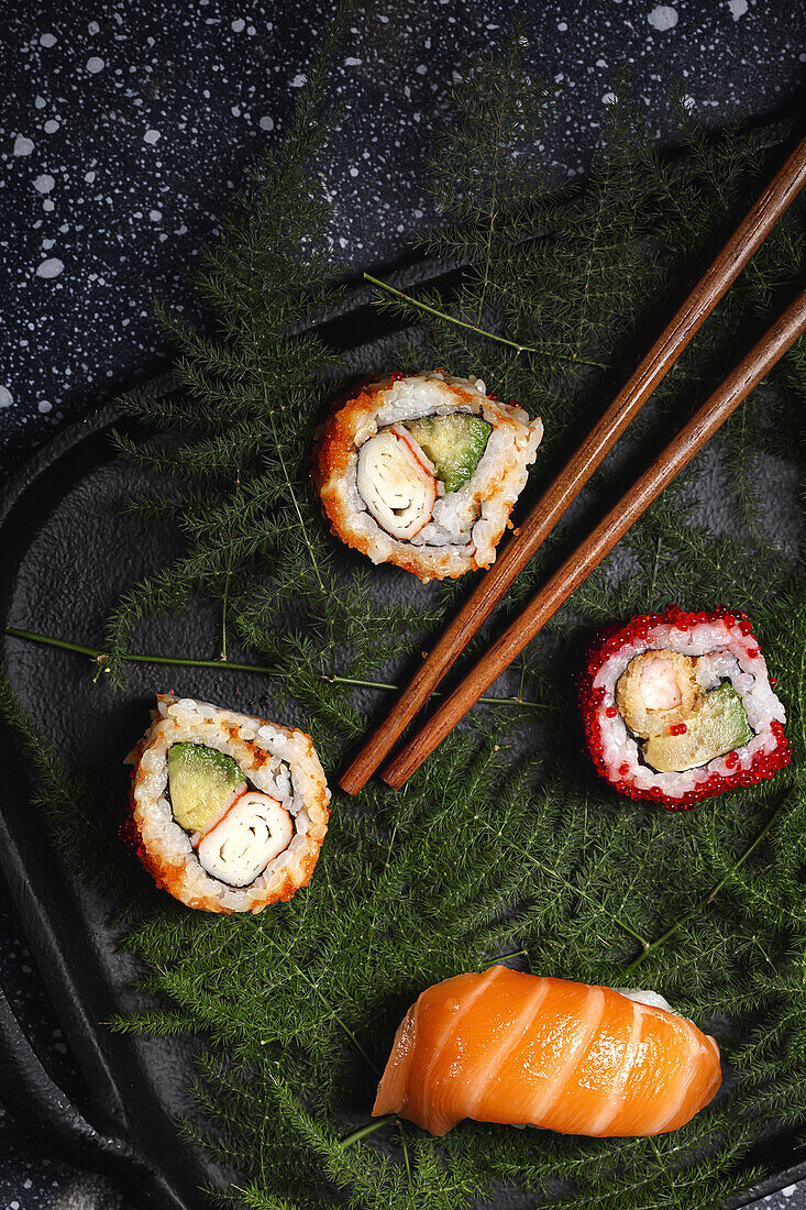 Top view composition of delicious fresh various sushi and bamboo chopsticks served on black platter on checkered cloth