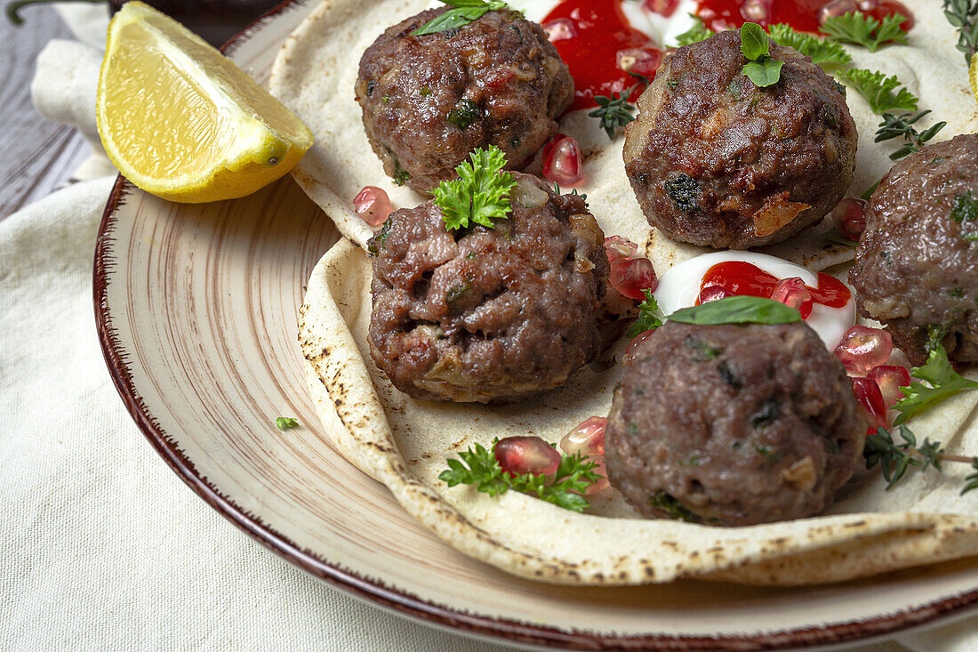 Traditional homemade beef and lamb meatballs with arabic bread, tomato sauce, pomegranate and aromatic herbs. Halal food