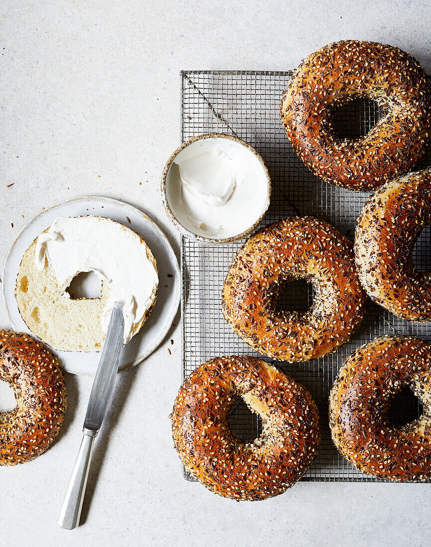 Draufsicht auf leckere gebackene Bagels mit Sesam auf einem Kühlregal neben Messer und Frischkäse auf dem Tisch