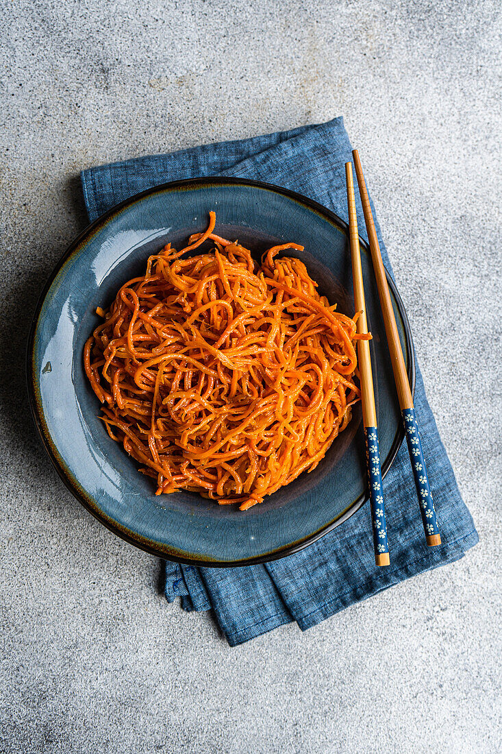 From above traditional spicy asian carrot salad served on ceramic plate and chopsticks on concrete background