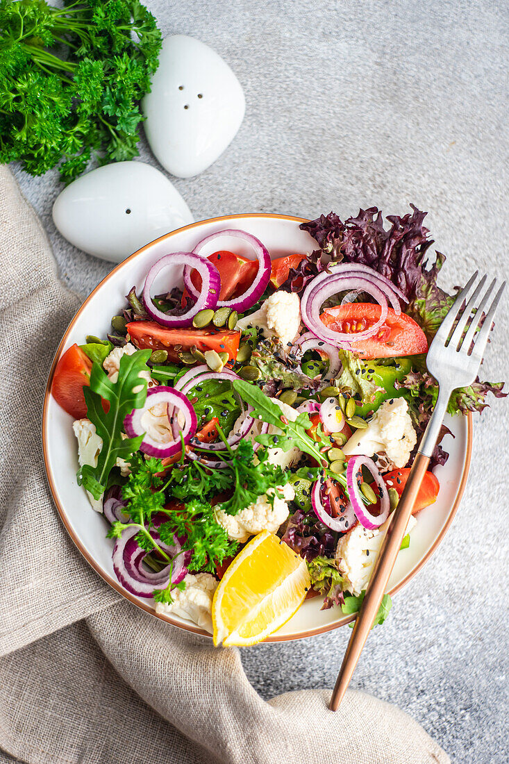 Organic vegetable salad with seasonal vegetables and herb mix with seeds and lemon in a bowl