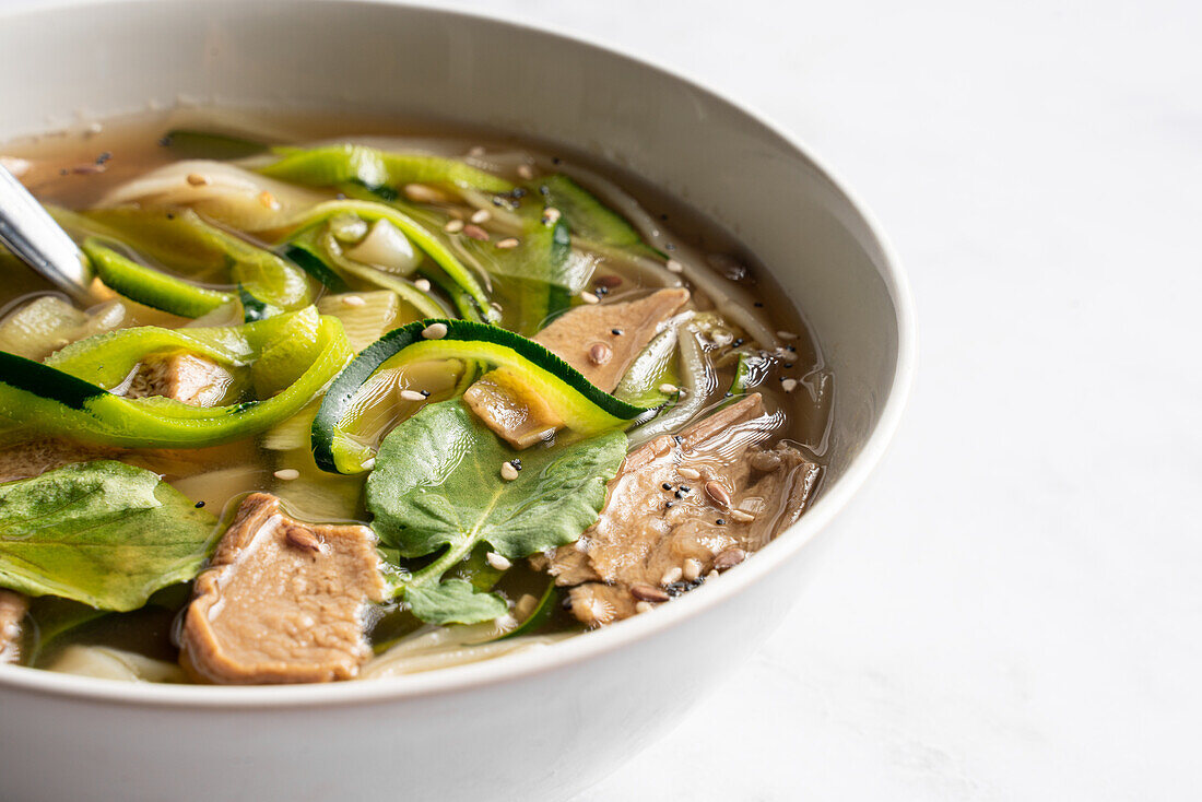 Bowl of traditional Vietnamese Pho bo noodle soup with basil leaves and lime placed on marble table in light room