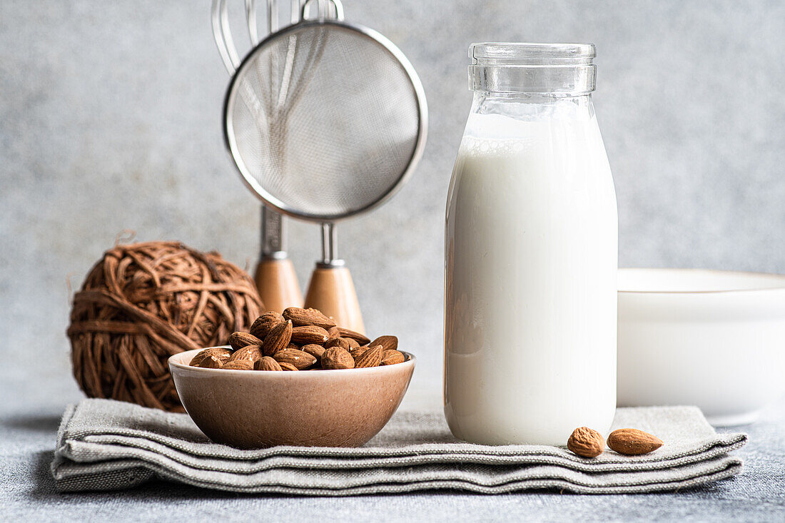 Bio-Mandelmilch in Glasflasche neben Keramikschale mit rohen Mandeln auf Steintisch in der Küche, bereit zum Kochen