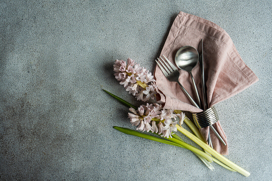 Frühlingshaft gedeckter Tisch mit Hyazinthenblüten neben Besteck auf grauem Betontisch für ein festliches Abendessen von oben