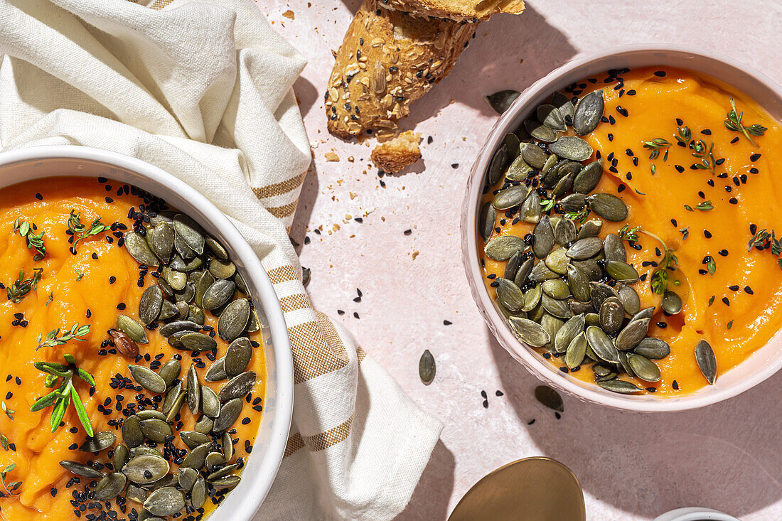 Top view of appetizing homemade pumpkin purees with seeds and herbs in bowls placed on table near crispy bread slices in kitchen