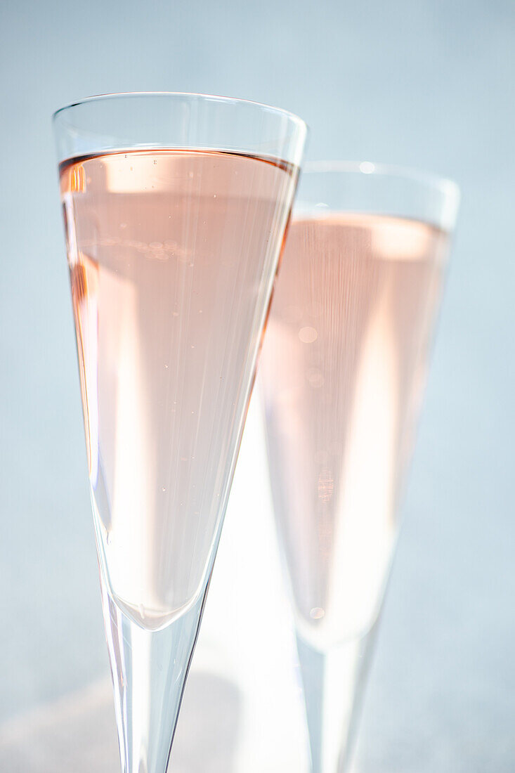 Rose sparkling wine or champagne in crystal glasses on light background in sunny day