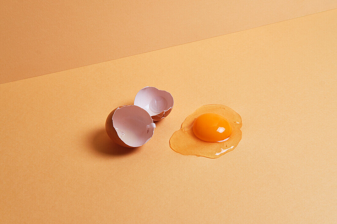 From above of fresh raw chicken egg placed on orange background in bright studio
