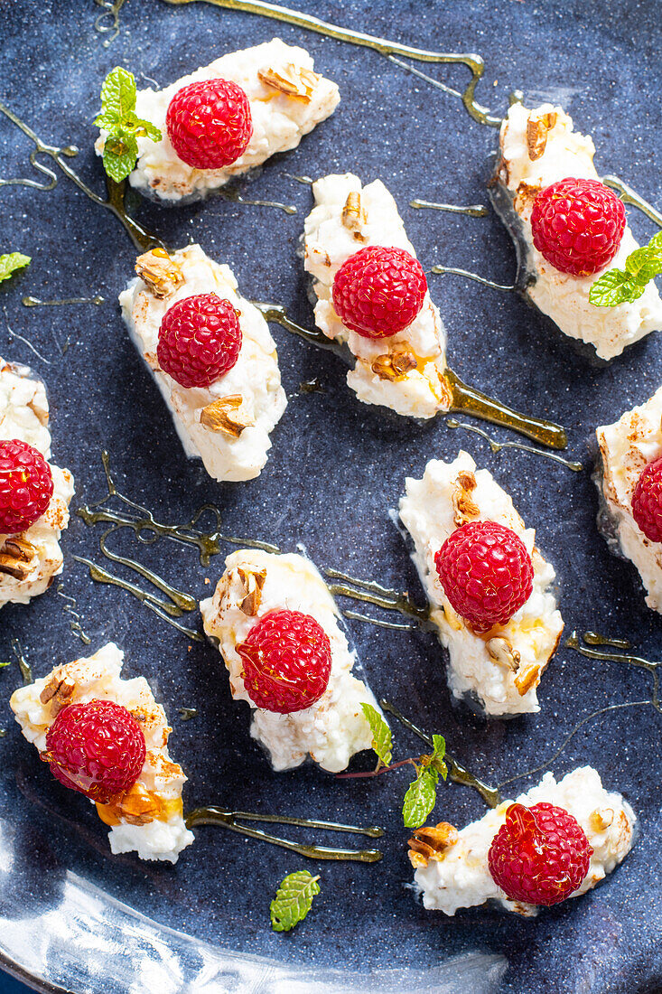 From above delicious sweet dessert with cream and raspberries served with mint leaves and nuts garnished by honey on blue plate