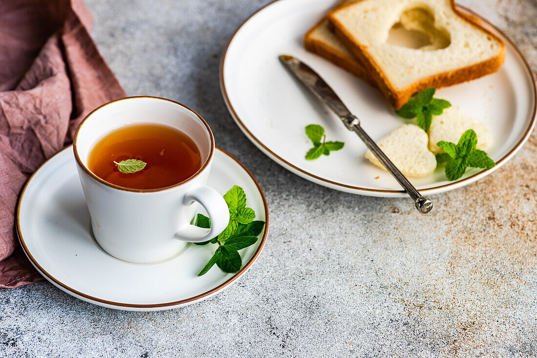 Tasse Tee mit Zitrone und Toasts in Herzform auf einem Betontisch