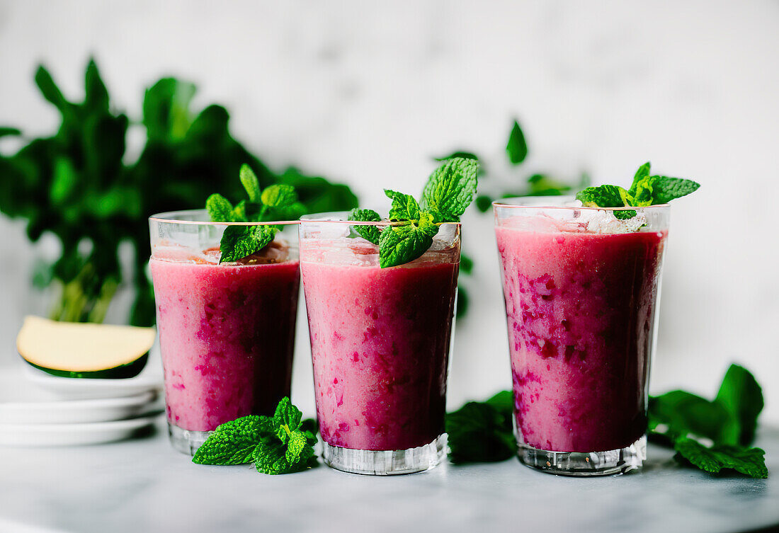 Transparent glasses filled with refreshing smoothies made of berries and mint leaves on table