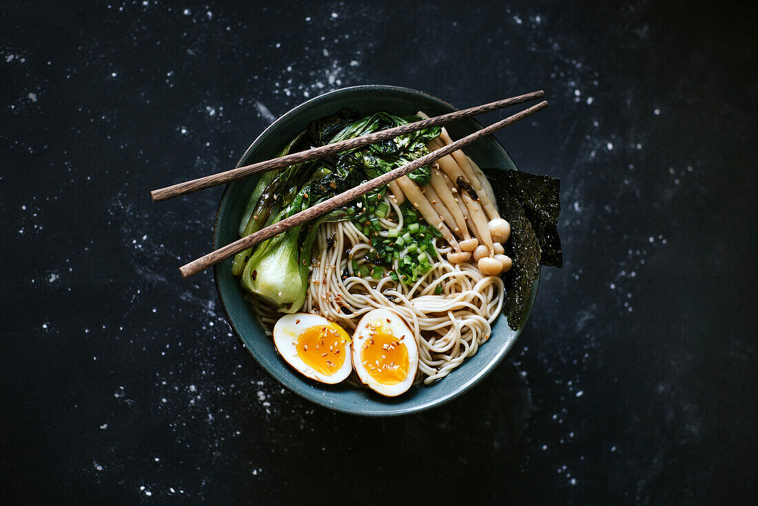 Keramikschüssel mit leckeren Ramen und Stäbchen auf dem Tisch (Draufsicht)