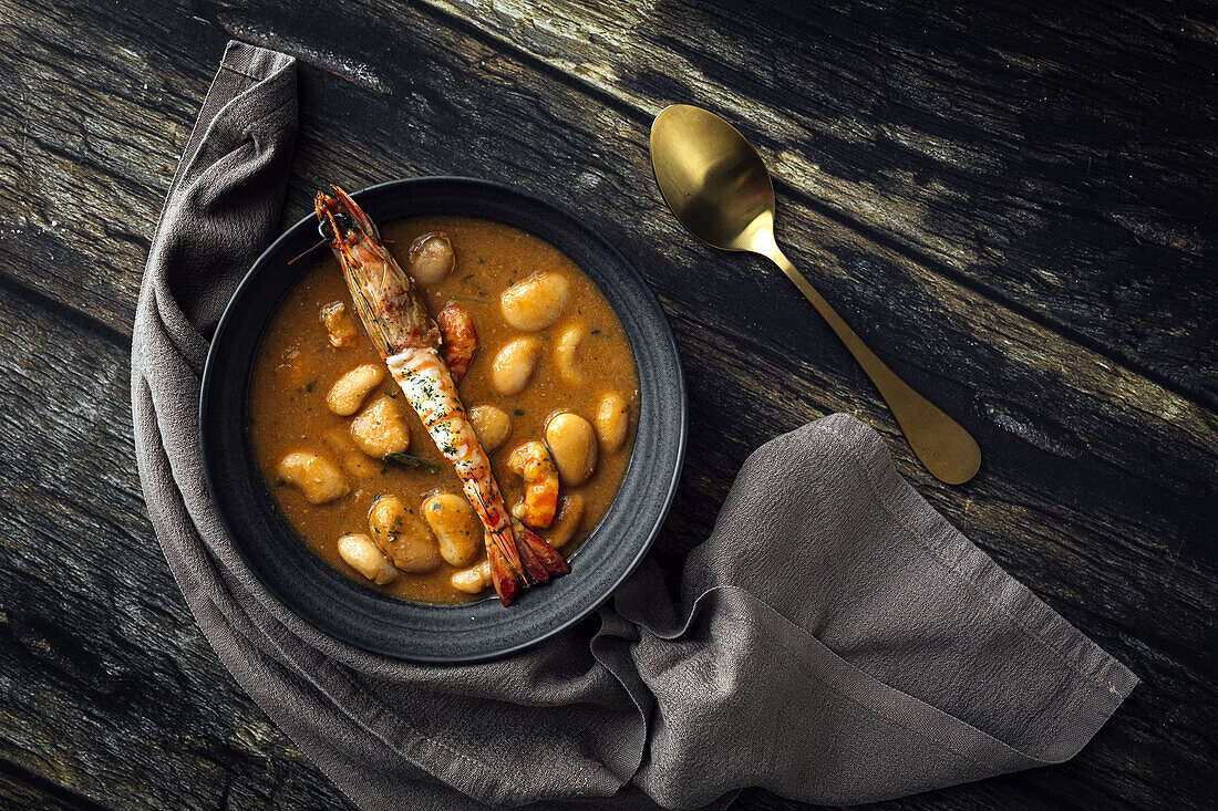 Appetitliche Cremesuppe mit weißen Bohnen und Langusten in einer Schüssel auf einem Holztisch in der Küche (von oben)