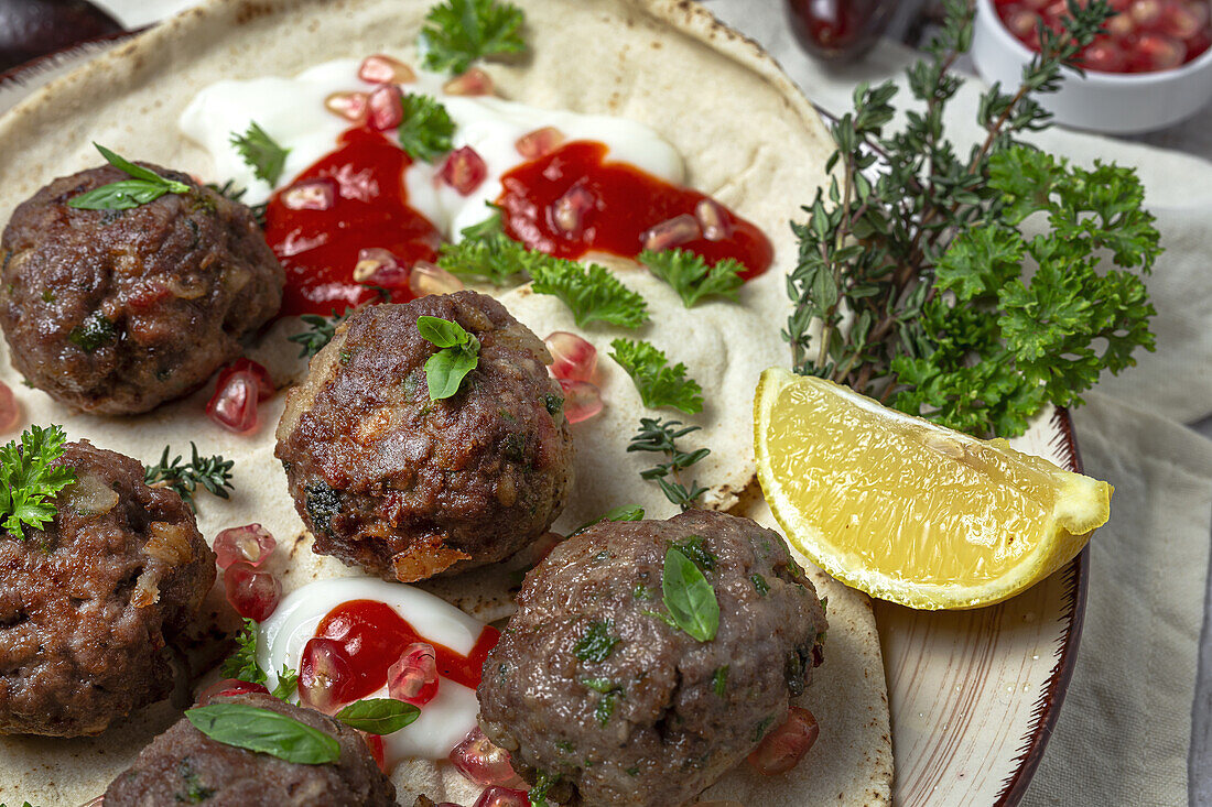 Traditional homemade beef and lamb meatballs with arabic bread, tomato sauce, pomegranate and aromatic herbs. Halal food