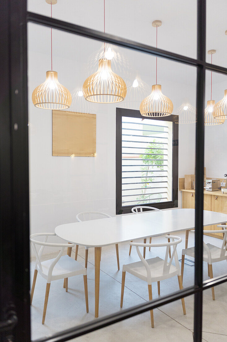 Durch Glas von weißen Stühlen und Tisch in der Nähe von Theke und Fenster in modernen hellen Cafeteria mit hängenden leuchtenden Lampen platziert