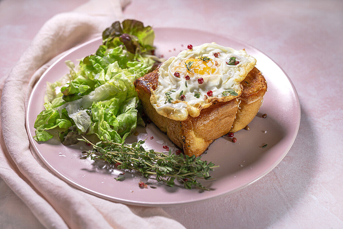 Spiegelei auf Brioche, serviert auf einem Teller mit frischem Salat zum appetitlichen Frühstück auf rosa Hintergrund