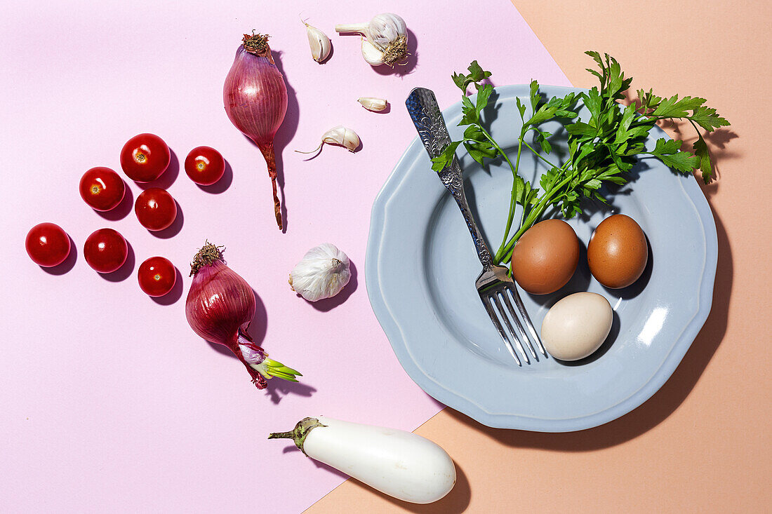 Top view of chicken eggs on plate with fork against fresh parsley sprigs and cherry tomatoes on two color background