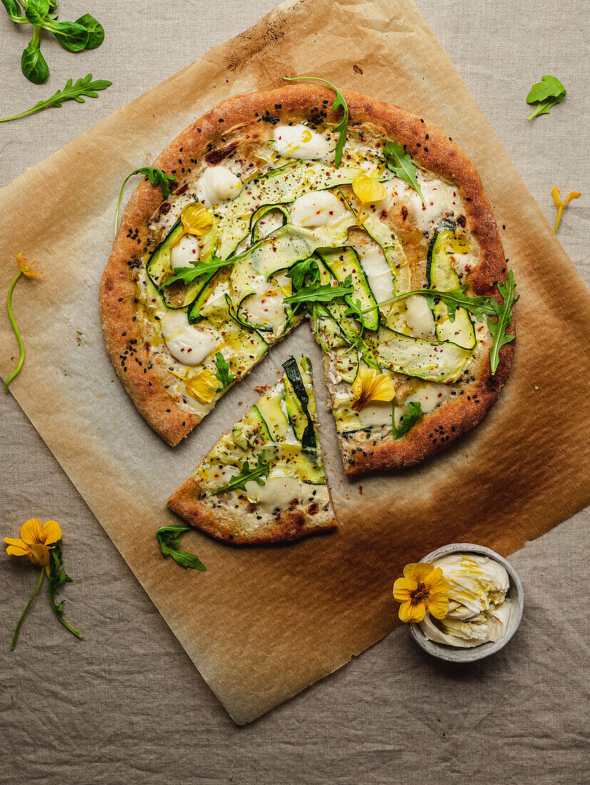 Draufsicht auf leckere Pizza mit Kürbisscheiben und Gewürzen mit frischen Rucolablättern auf Pergamentpapier auf beigem Hintergrund