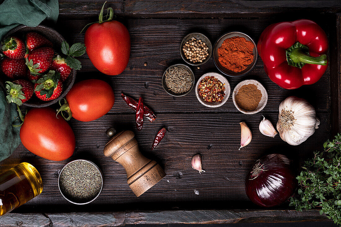 Draufsicht auf frische reife Tomaten und Erdbeeren auf Holztisch mit verschiedenen Gewürzen und Zutaten für Gazpacho-Suppenrezept