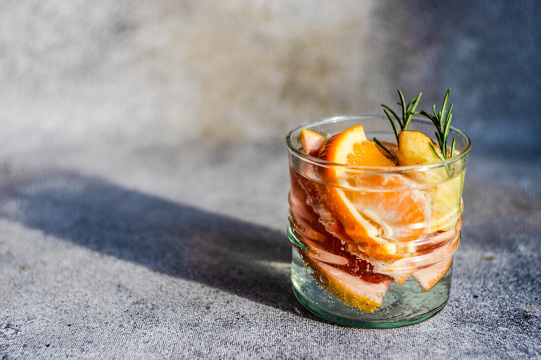 Summer tropical cocktail of vodka and sprite with ripe fruits and rosemary on grey background