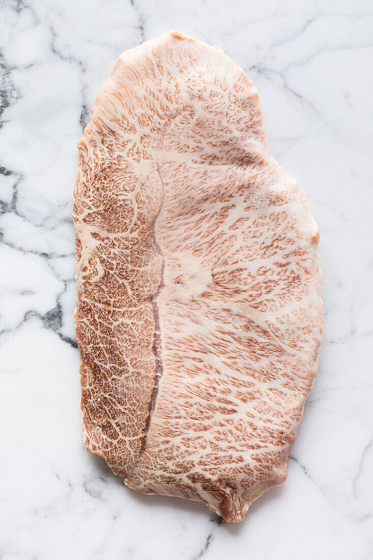 Top view of traditional Japanese uncooked kobe prefecture wagyu beef placed on marble table in light room during cooking preparation