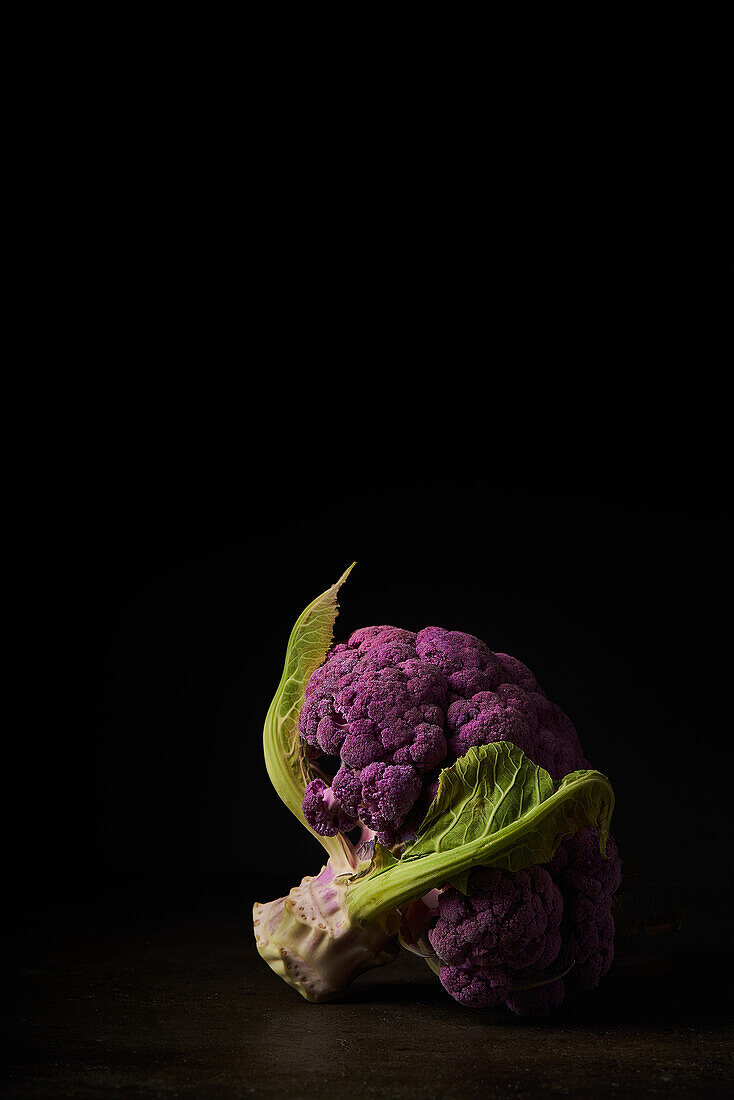 Tasty purple broccoli placed on wooden table on black background in dark studio