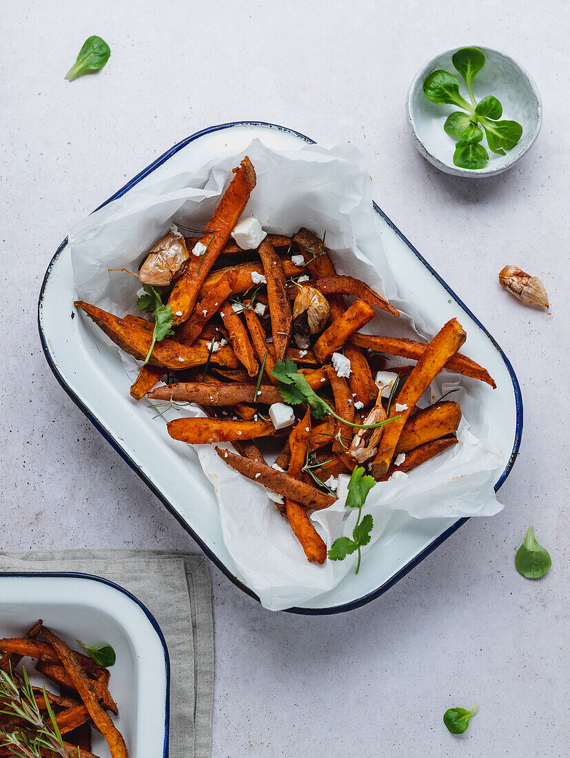 High angle of delicious sweet potato fries with sour cream and herbs served on table