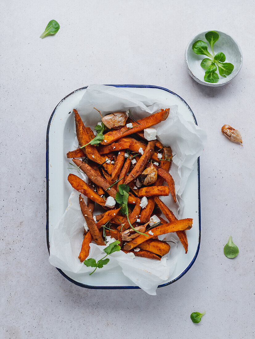 High angle of delicious sweet potato fries with sour cream and herbs served on table