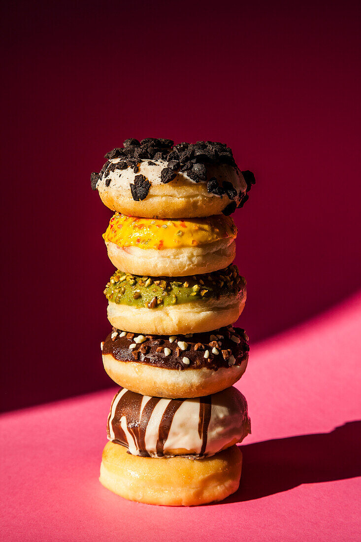 Tower of donuts of different colors and flavors on pink background
