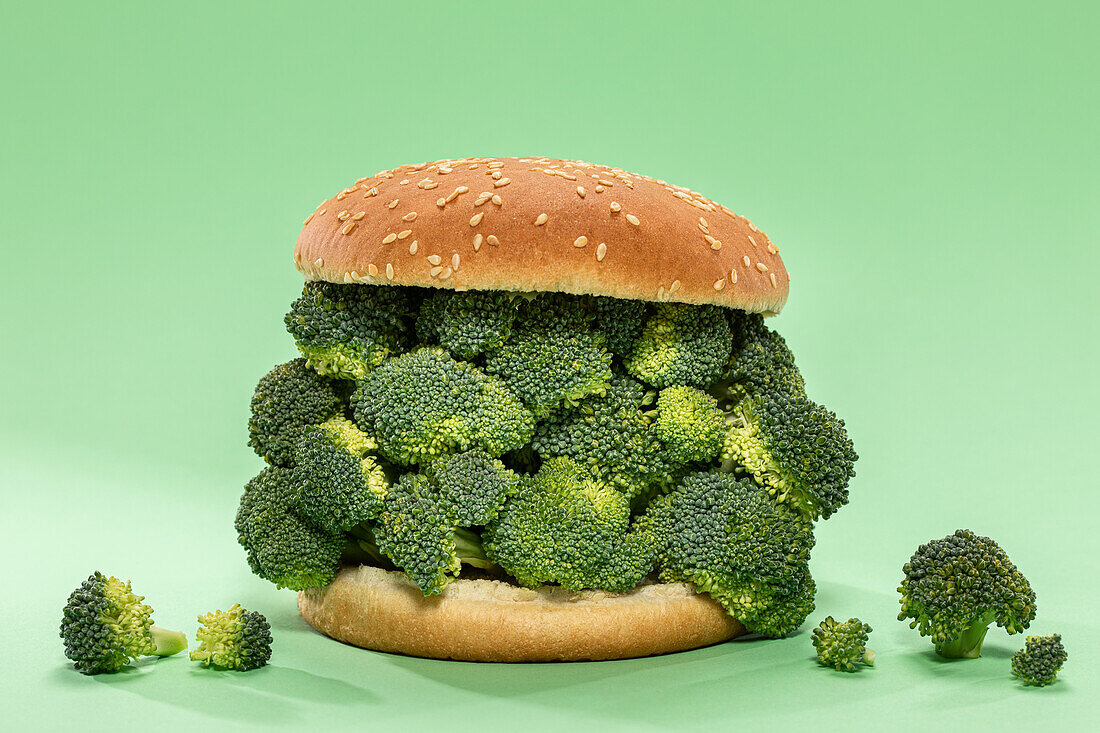 Halves of burger bun with bunch of raw broccoli served on green background during healthy lunch