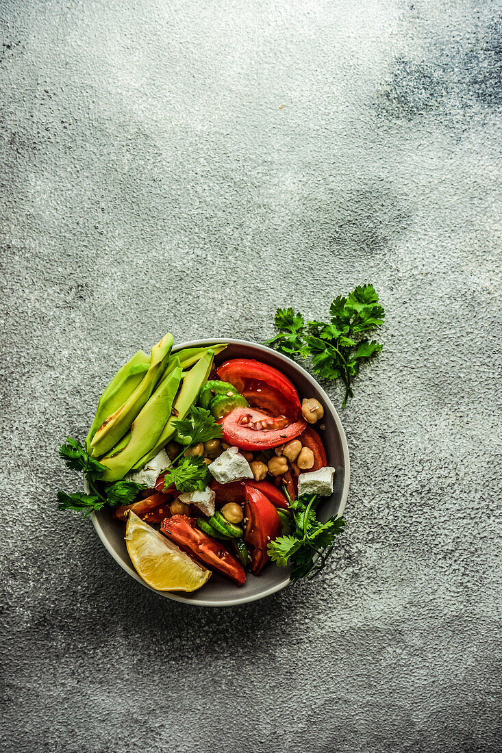 Von oben gesunder Salat mit biologischem Gemüse der Saison und Avocado auf einem Betontisch serviert