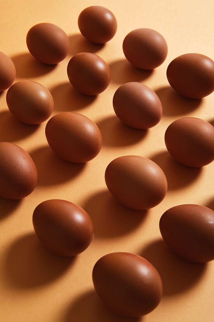 Nahtloser Hintergrund mit braunen Eiern, die in Reihen auf einem orangefarbenen Tisch im Studio platziert sind