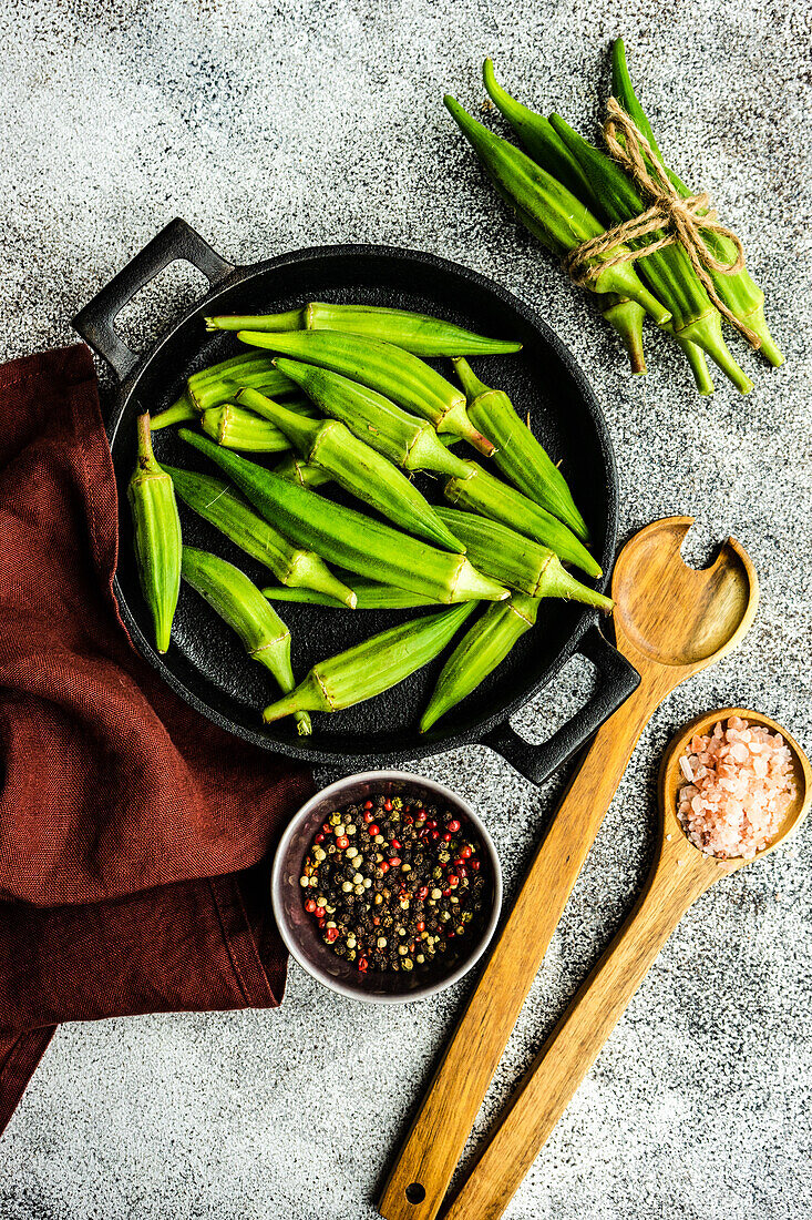 From above preparation for cooking of bamia vegetable with pepper and himalayan salt on concrete background near napkin cloth