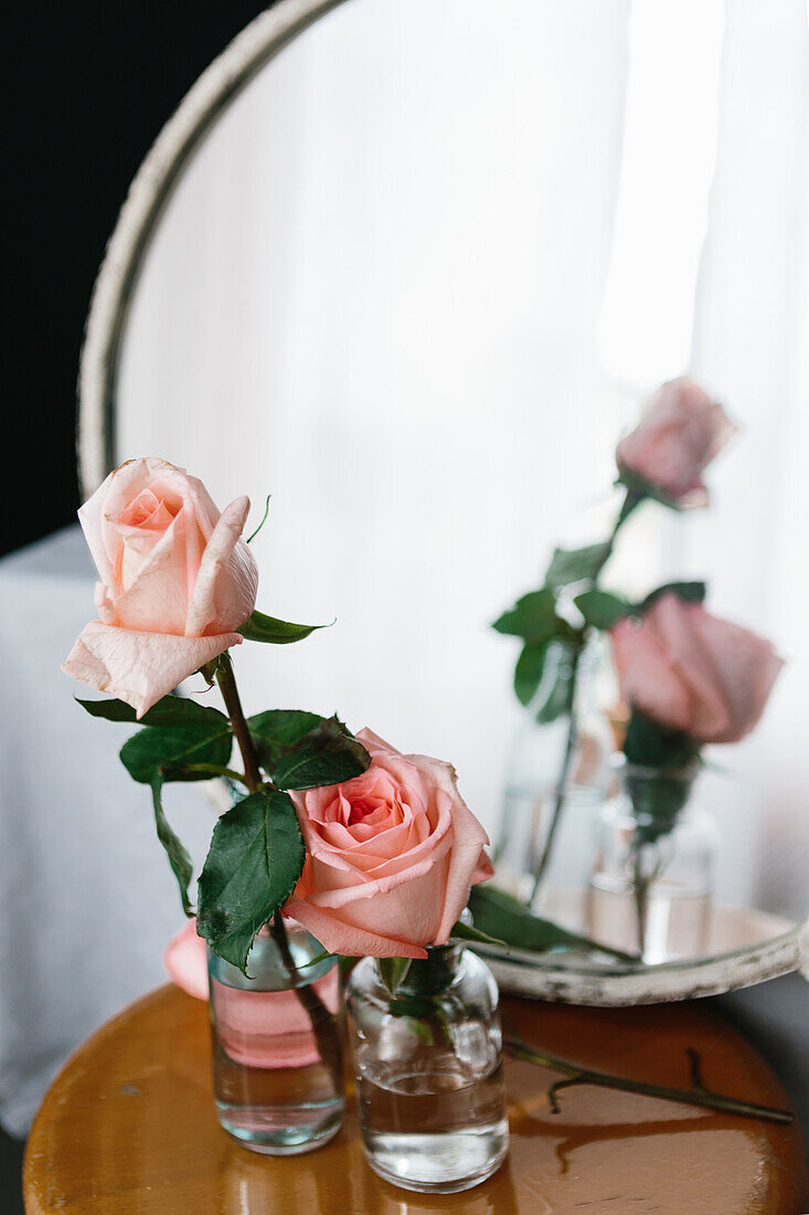 Rosa Rosen in Glasvasen auf einem Holztisch vor neutralem Hintergrund