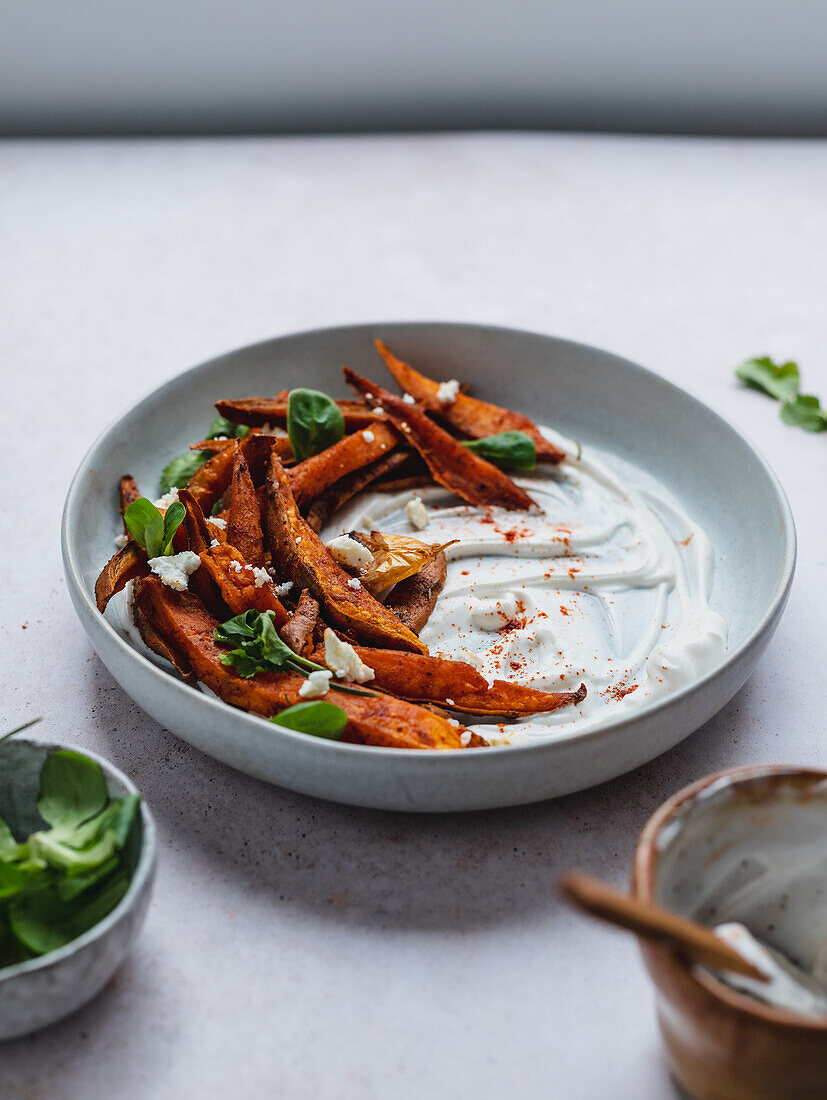 High angle of delicious sweet potato fries with sour cream and herbs served on table