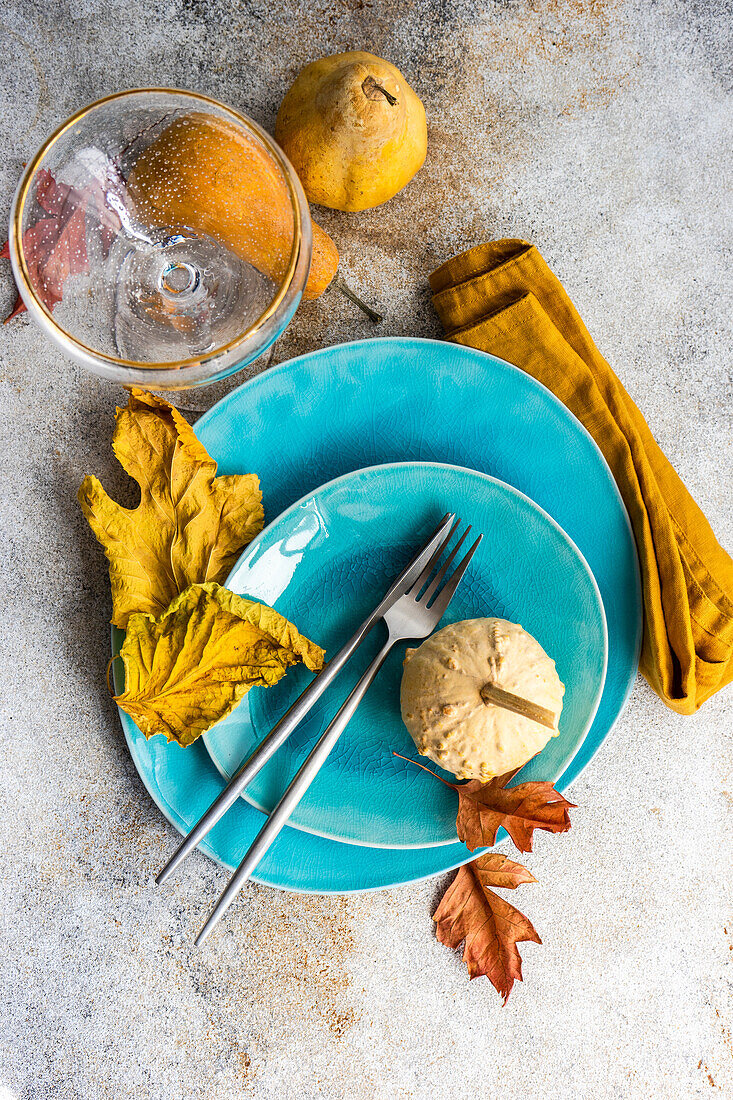 Autumnal place setting with blue ceramic dinnerware and seasonal decoration on concrete table