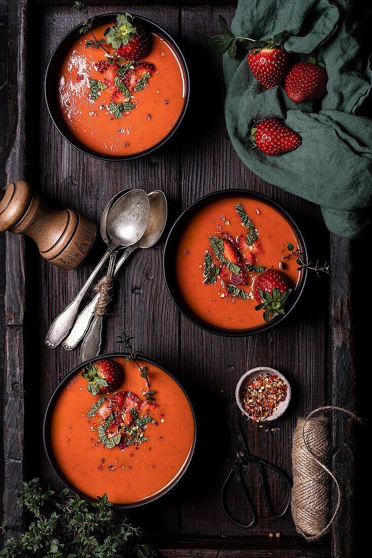 Komposition von oben mit köstlicher hausgemachter Tomaten-Erdbeer-Gazpacho-Suppe, serviert in Schalen auf einem rustikalen Holztisch