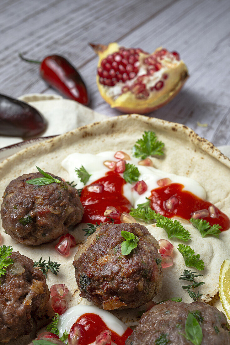 Traditional homemade beef and lamb meatballs with arabic bread, tomato sauce, pomegranate and aromatic herbs. Halal food