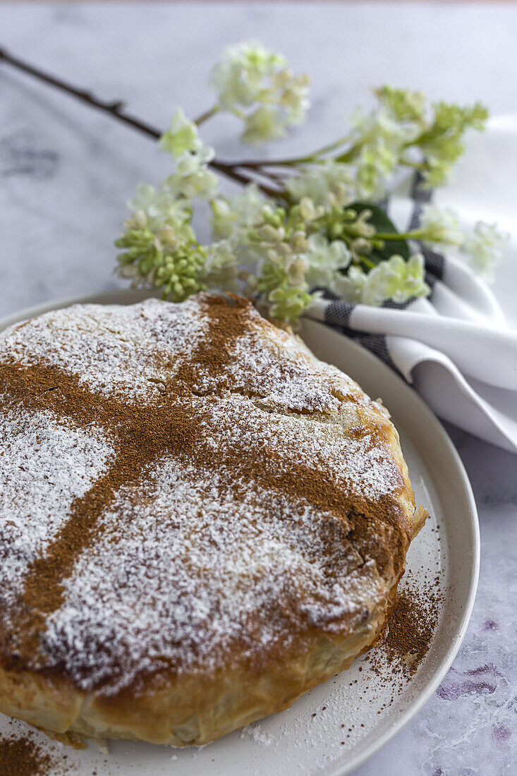 Appetitliche Bastilla mit aromatischen Gewürzen auf dem Tisch in der Nähe eines Blumenzweigs während des Ramadan-Festes