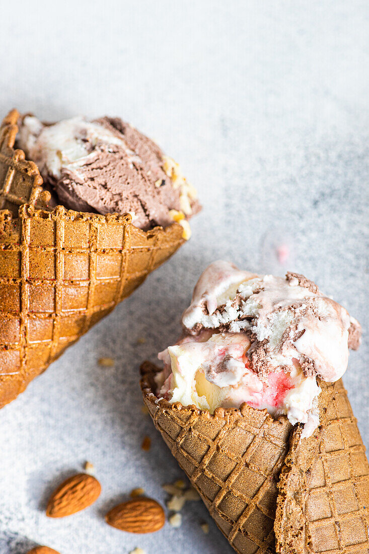 From above waffle cones with cherry and chocolate ice cream on concrete background