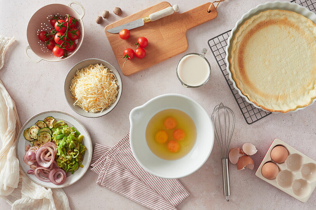 Top view of various fresh ingredients for quiche placed near empty crust on table in kitchen at home