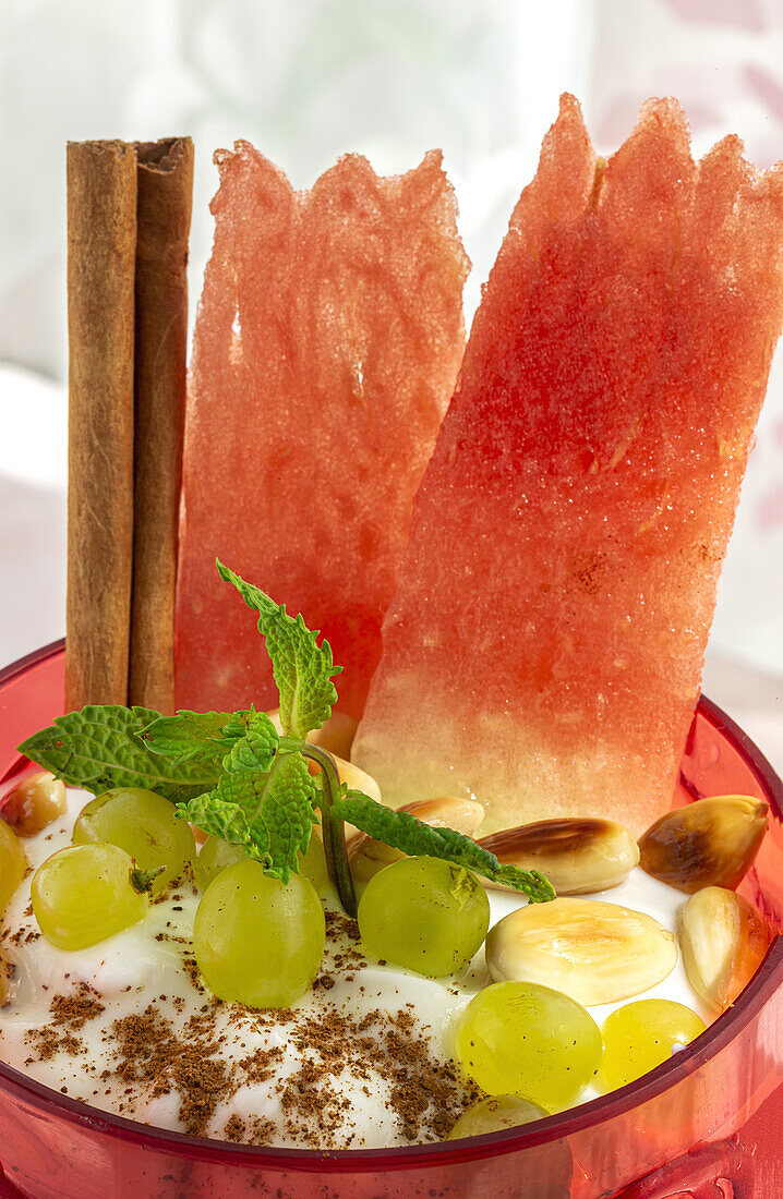 Von oben: Joghurt mit Trauben und Wassermelone, garniert mit Zimtstange und Minze, serviert auf einem Sommertisch