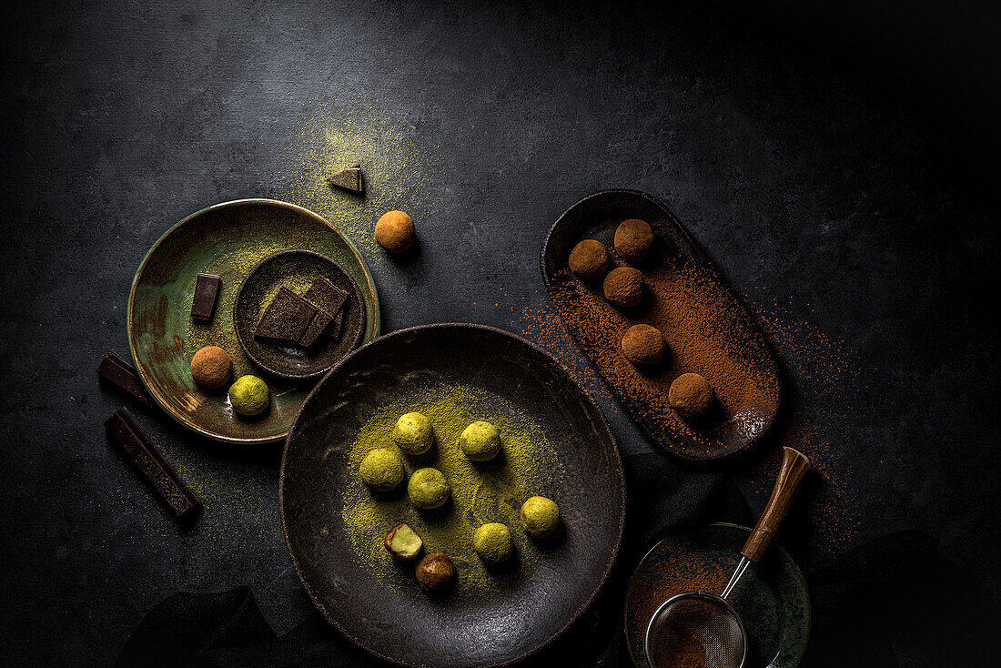 Overhead big plate with green truffle Matcha and plate with brown truffles balls with powder and strainer and chocolate pieces