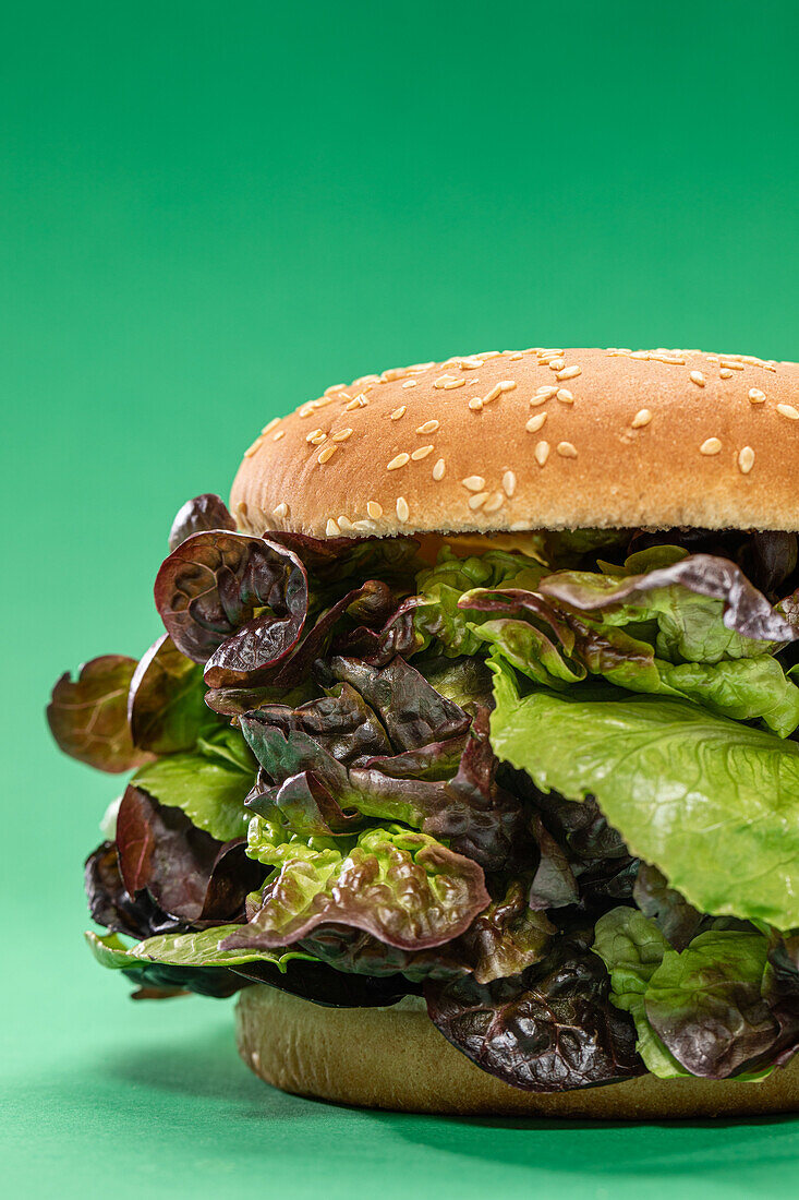 Fresh burger bun with bunch of fresh mesclun leaves as concept of healthy food against green background