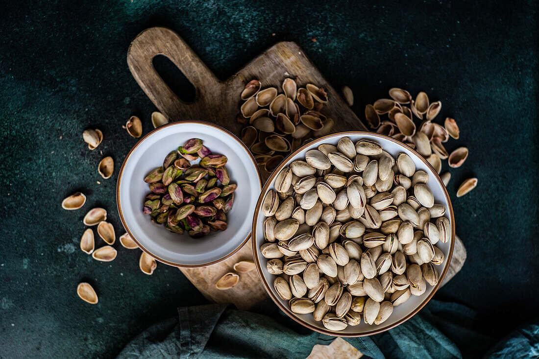 From above organic and raw pistachio nuts in the bowls on green table background