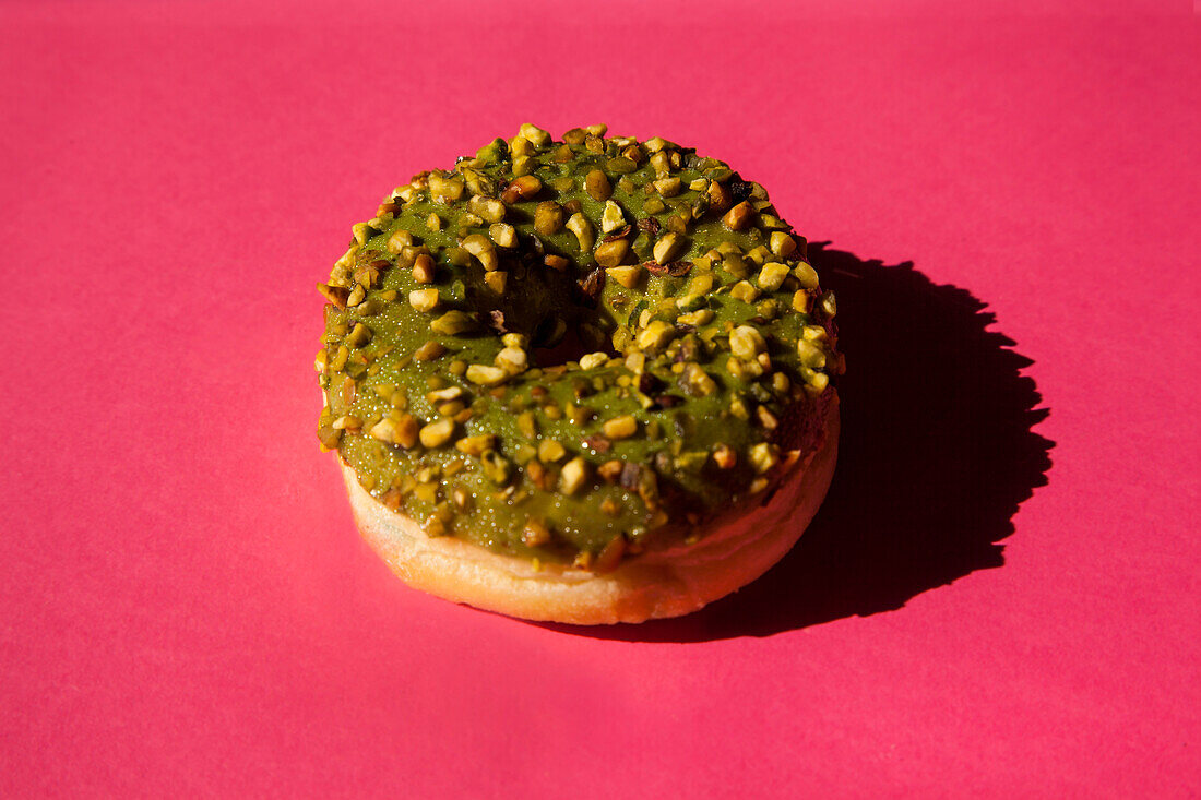 Draufsicht auf einen mit grünem Zucker bestrichenen Donut mit Nüssen auf rosa Hintergrund