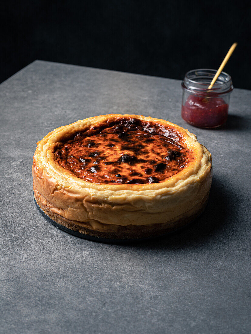 Yummy homemade sweet cheesecake placed against jar with jam on gray table