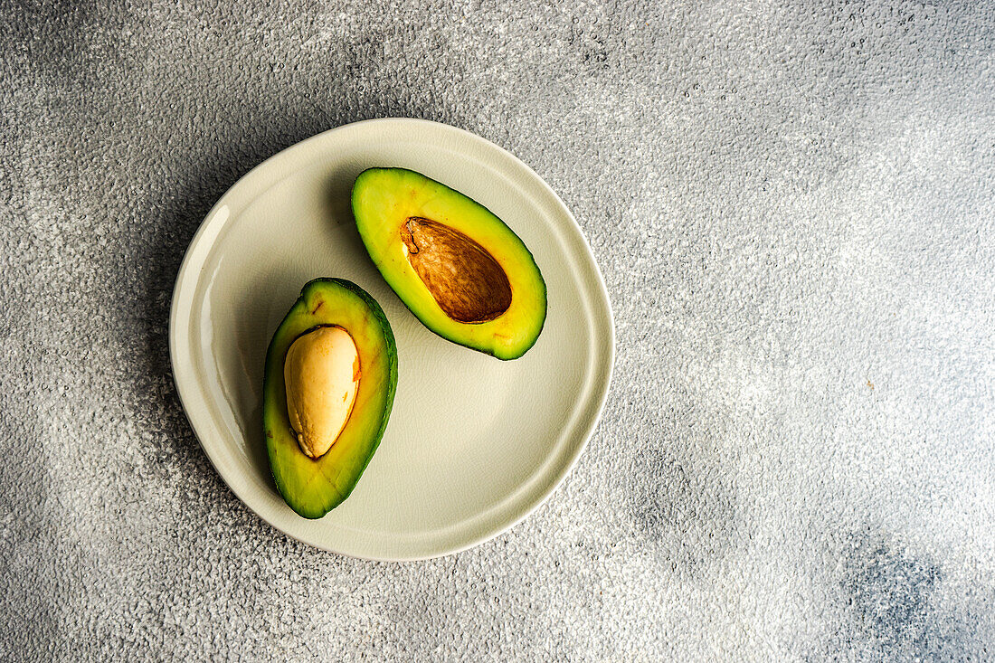 From above half of avocado on the plate on grey concrete background