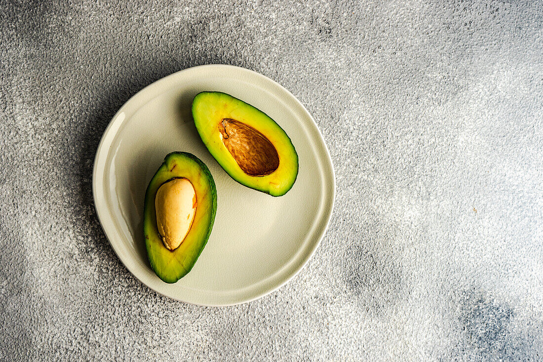 Von oben eine halbe Avocado auf einem Teller auf grauem Betonhintergrund